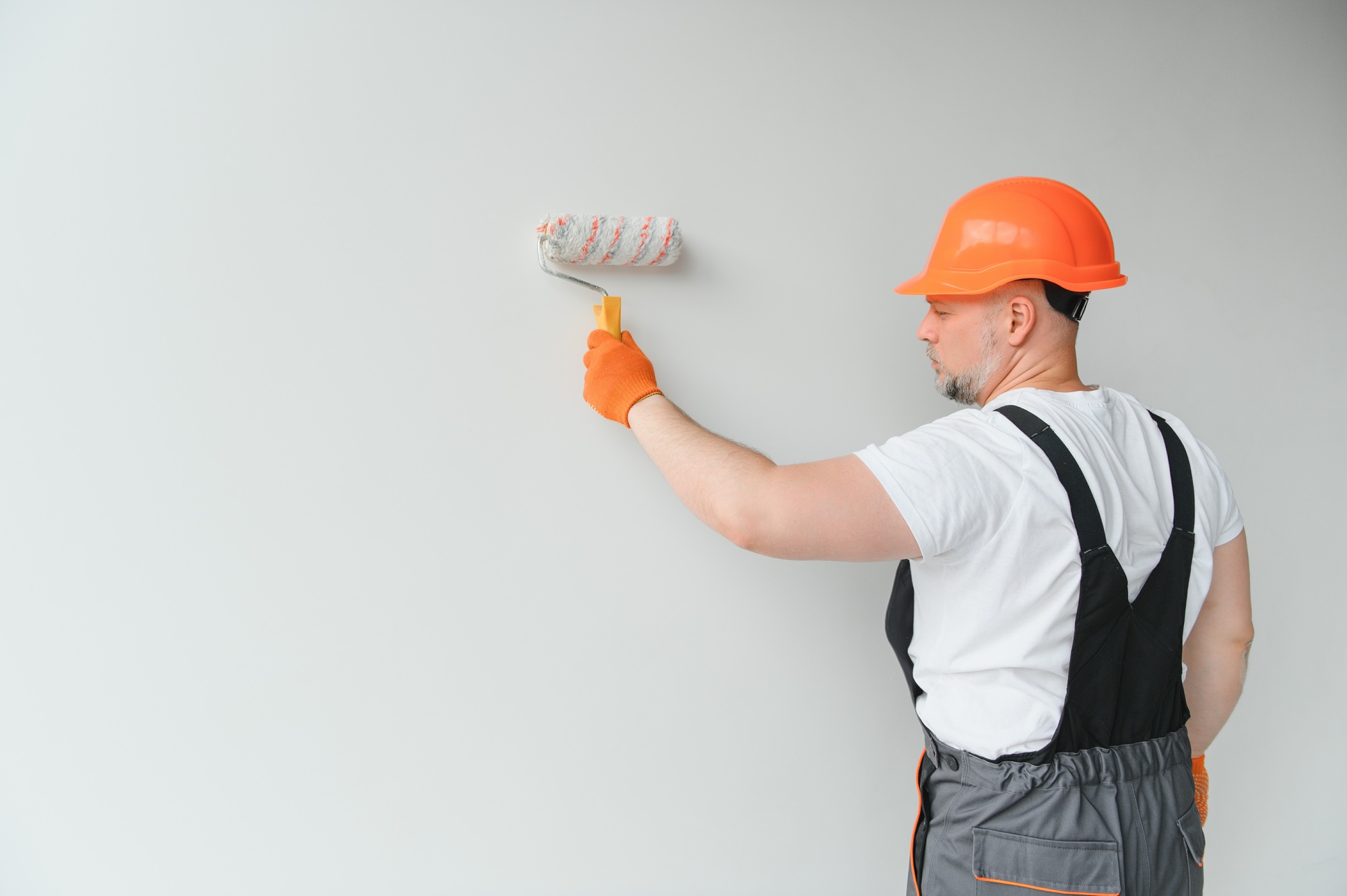 Painter man painting the wall in home, with paint roller and white color paint.